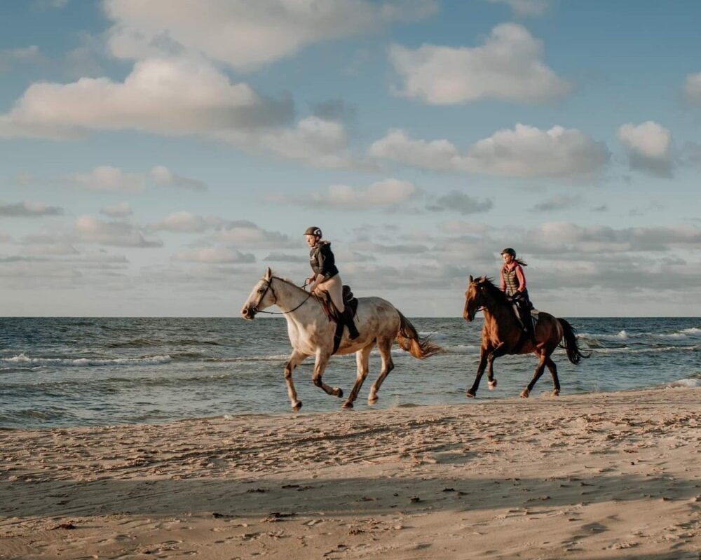 Para ludzi jadących na galopujących koniach po piaszczystej plaży.